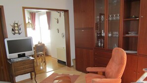 A living room with a television, wooden furniture, a cushioned chair, and a cabinet with glass doors. - Holiday house without everyday noise (Altomünster)