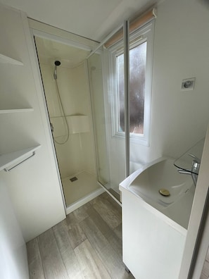 Un baño pequeño con ducha, un lavamanos con cristal y una ventana.