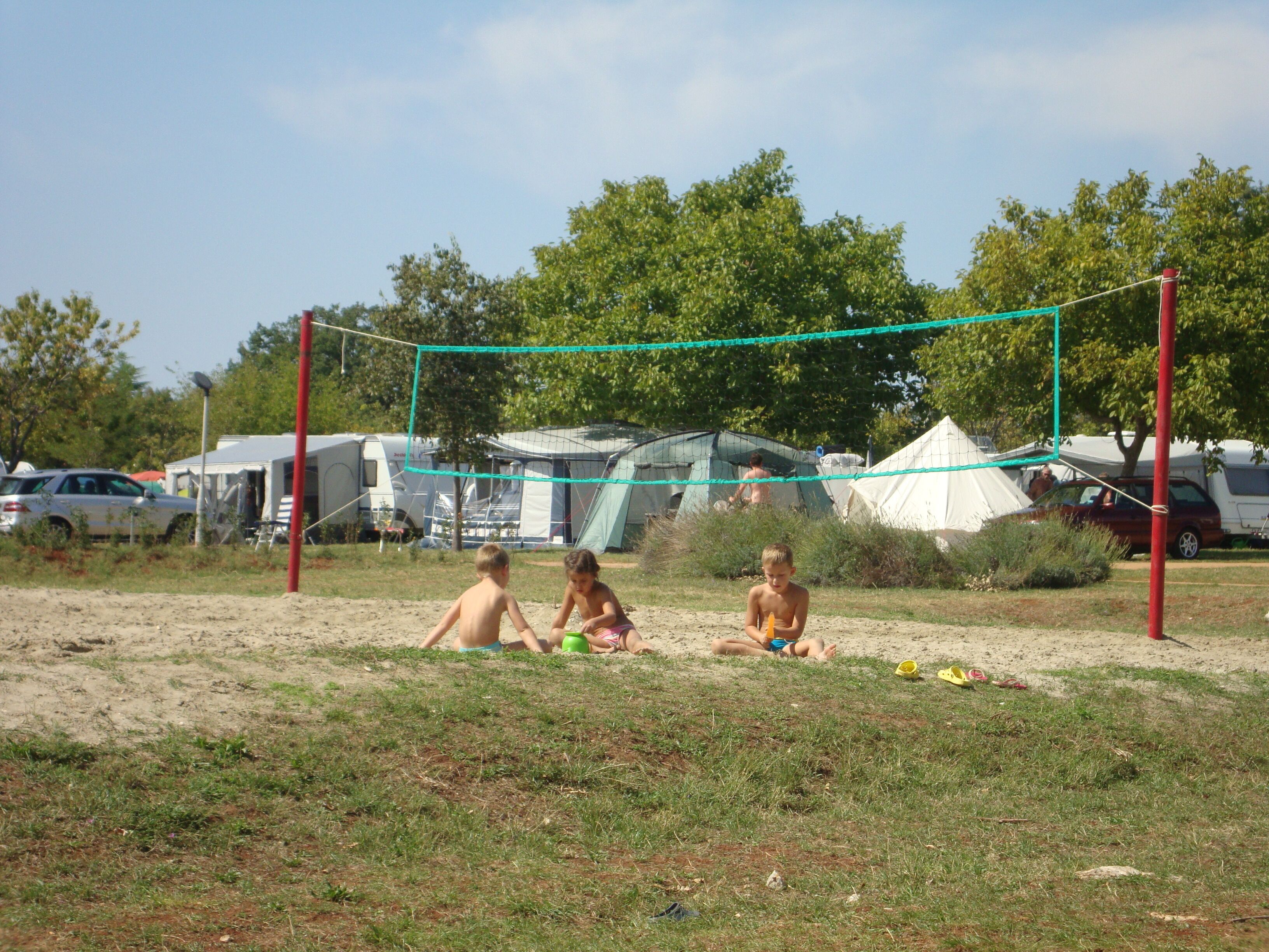 Un terrain de beach-volley sablonneux, avec un filet, entouré de tentes et de véhicules.