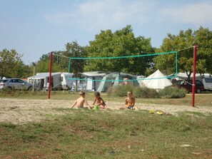 Una cancha de voleibol de arena con red, rodeada de tiendas de campaña y vehículos.