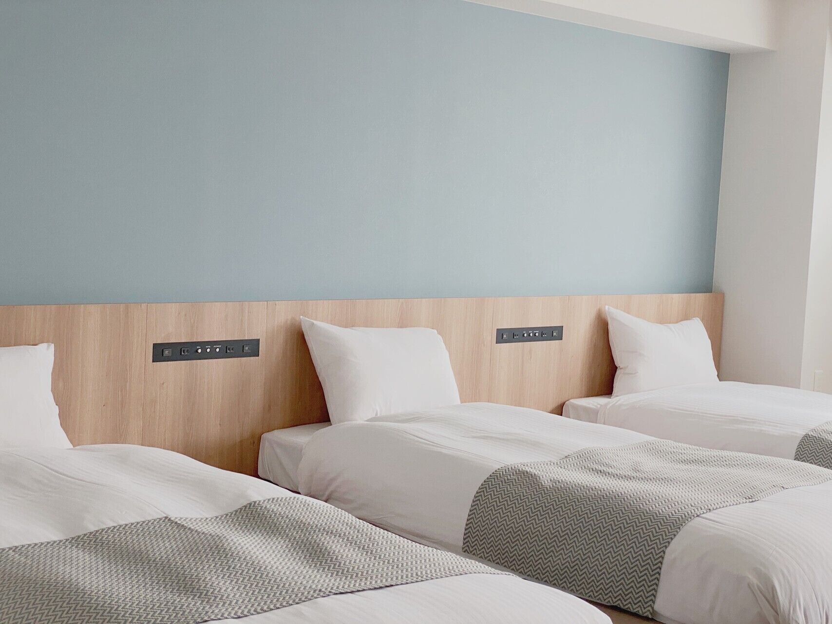 A hotel room with three beds, a wooden headboard, and a control panel above the beds.
