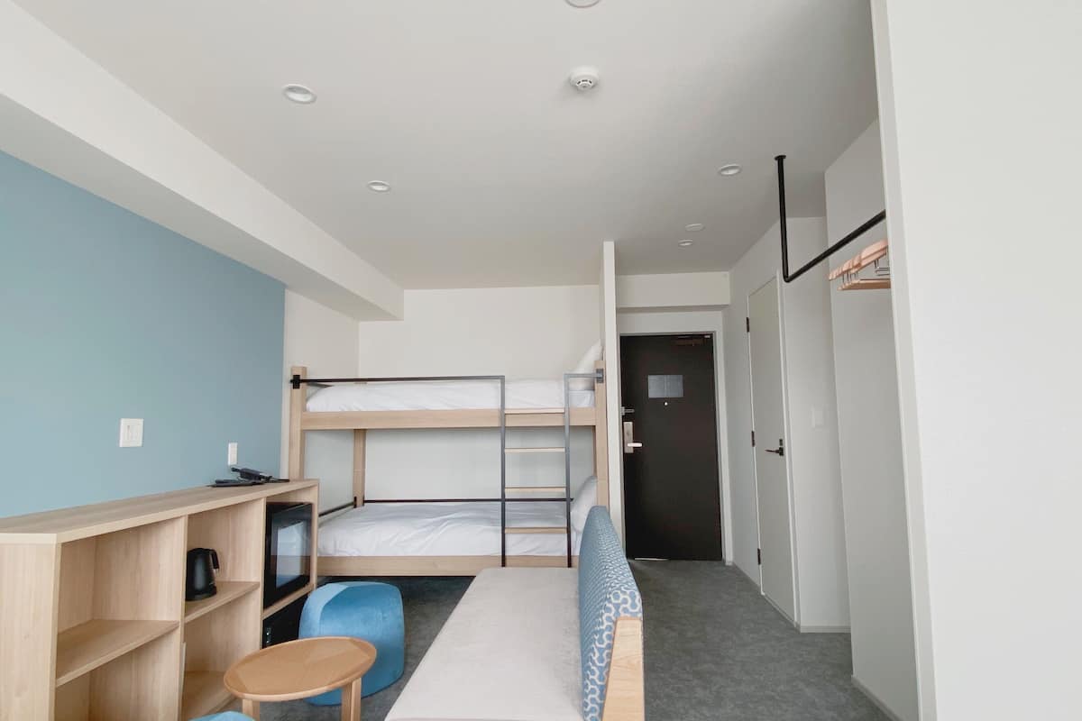 A compact hotel room with bunk beds, a desk with a chair, a small table, and a wardrobe.