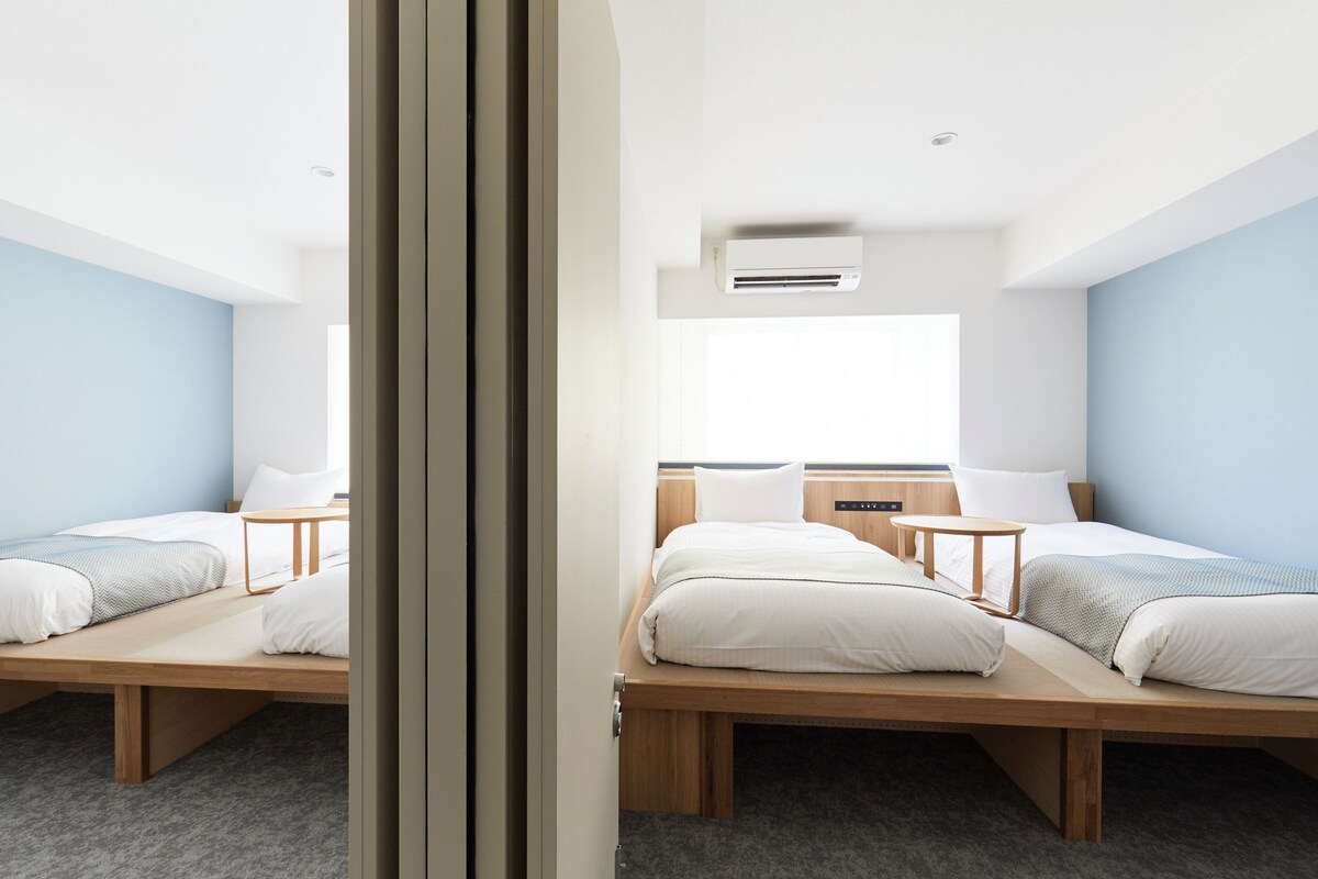 A room with two beds, a window, and an air conditioning unit.