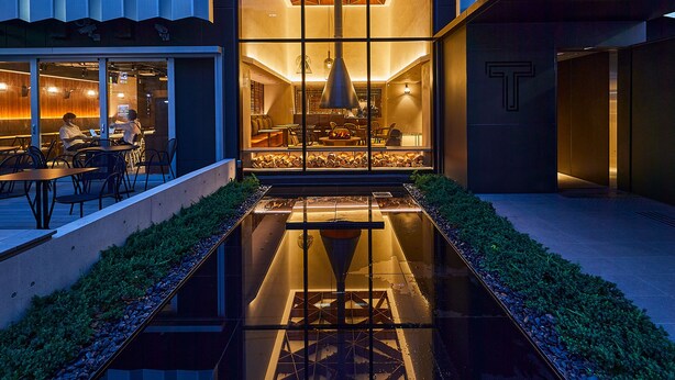 Un edificio moderno con fachada geométrica, una fuente de agua reflectante e interior con un llamativo logo 'T'.