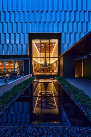 Un bâtiment moderne à la façade géométrique, agrémenté d’un élément aquatique réfléchissant et doté d’un intérieur où le logo en forme de « T » est particulièrement visible.