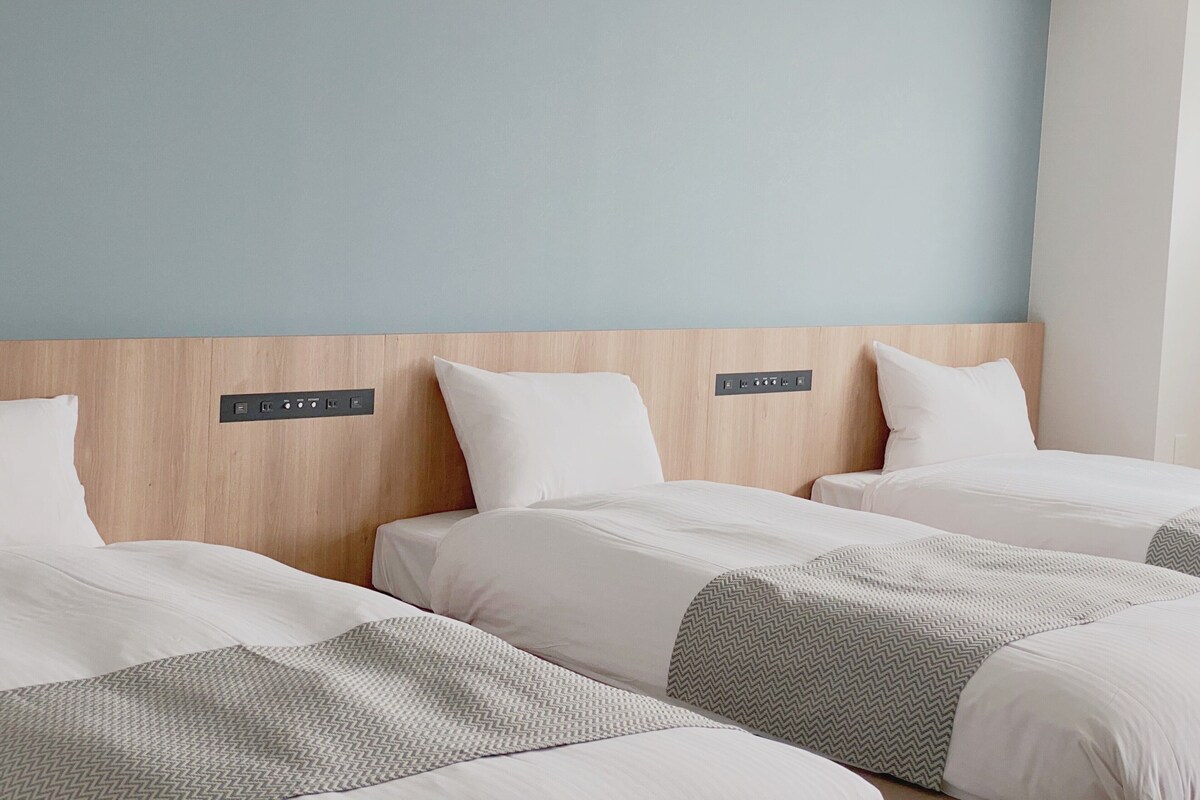 A hotel room with three single beds, a wooden headboard, and a control panel above each bed.