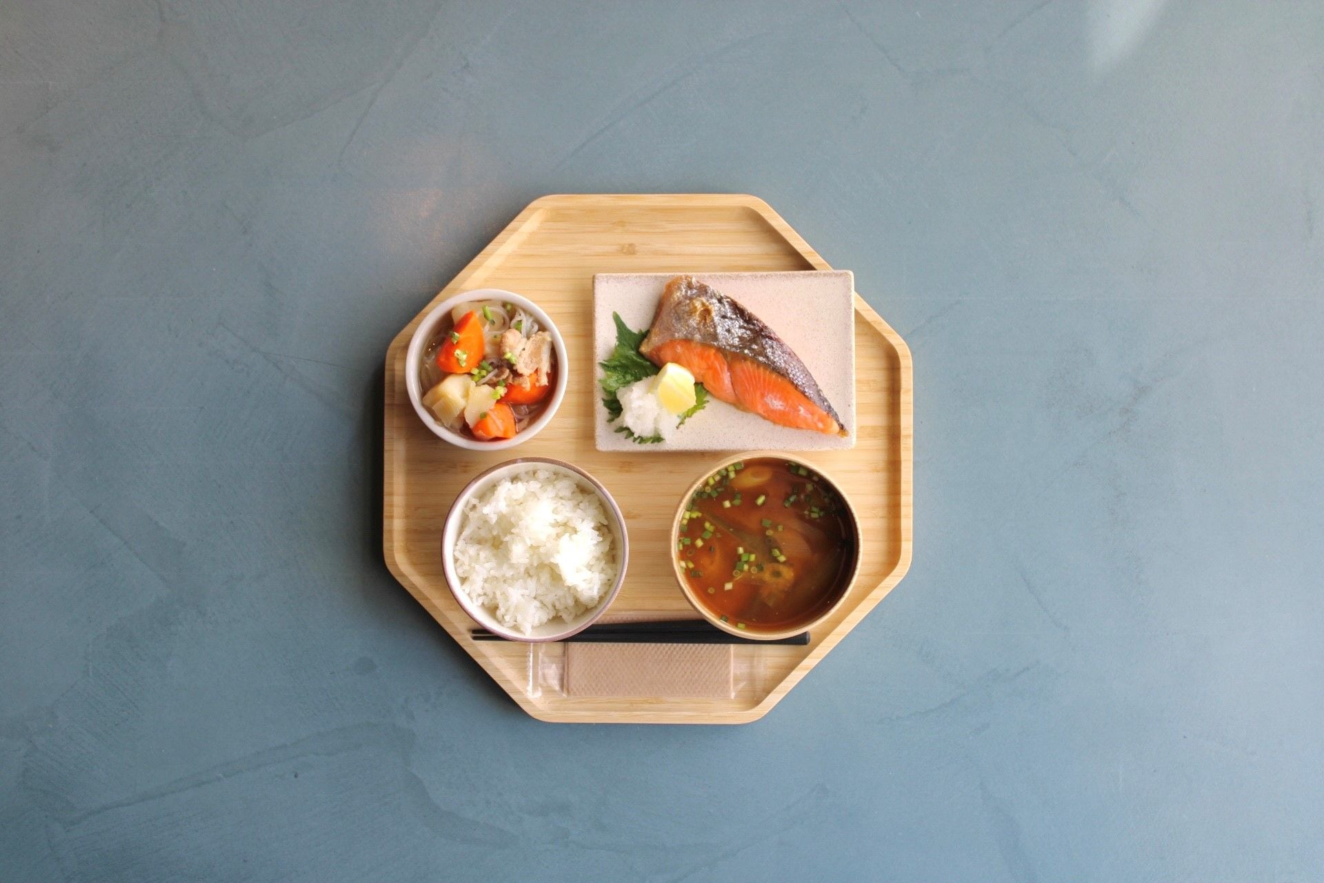 A wooden tray with a bowl of soup, a piece of fish, a bowl of rice, and a small dish of pickled vegetables.