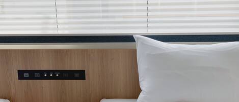 Habitación de hotel con cabecera de madera, panel de control con botones y cama con ropa blanca.