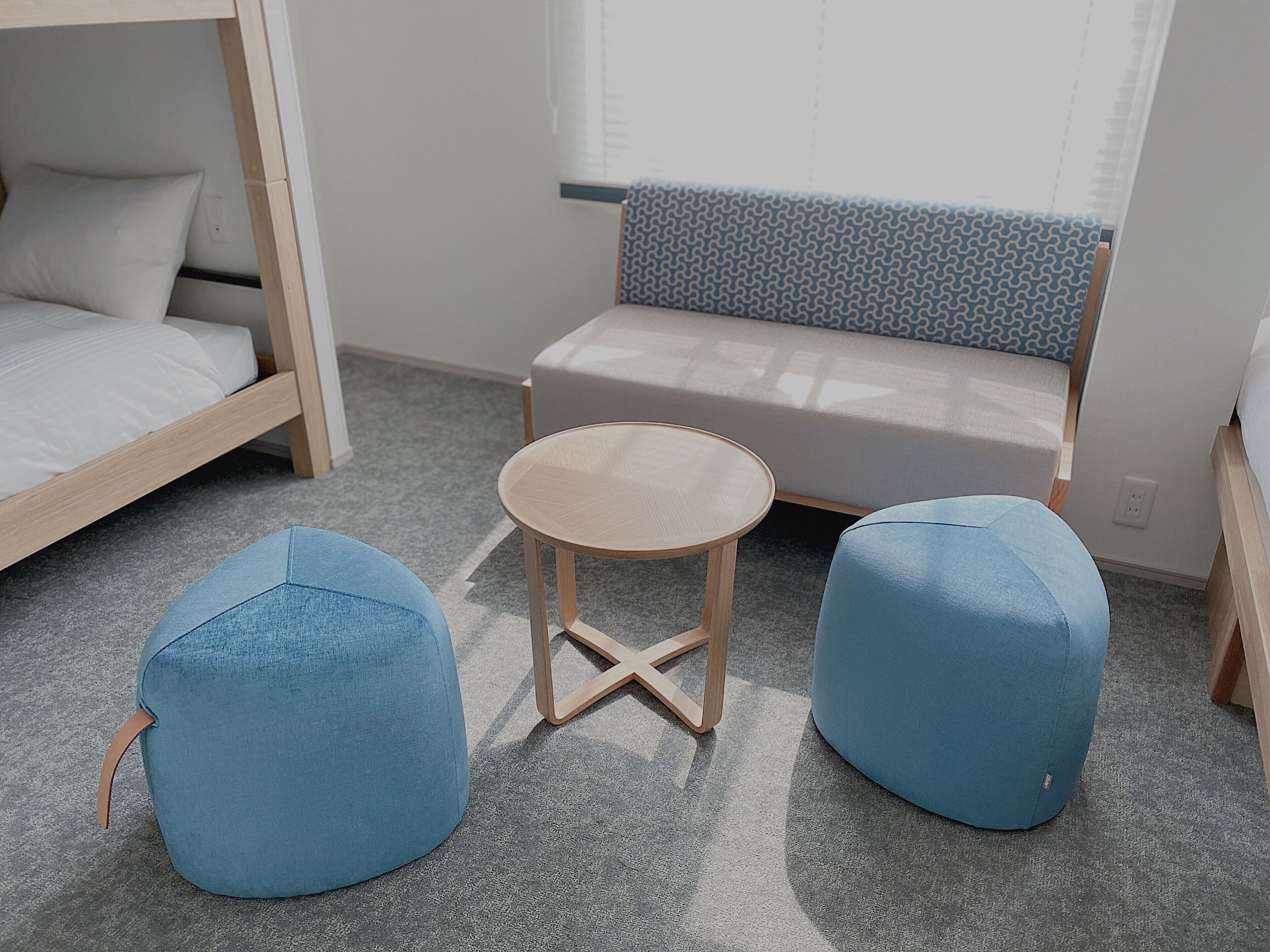 A cozy room with a bunk bed, a small round table, and two blue ottomans.