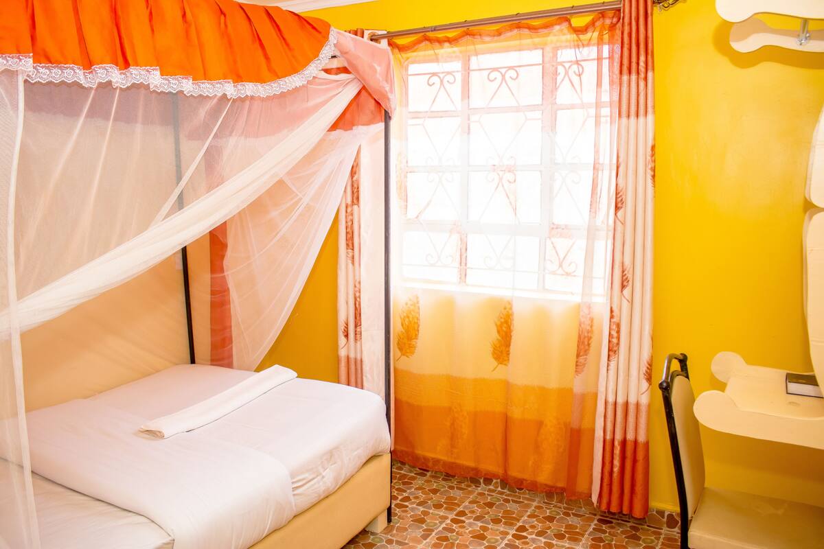 A room with a bed, a window with curtains, a sink, and a tiled floor.