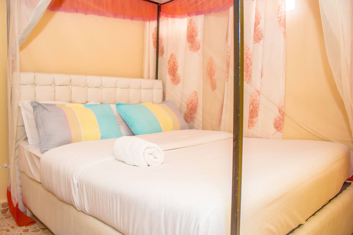 A bed with a canopy, striped pillows, and a rolled towel.