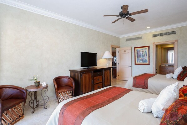 Habitación de hotel con dos camas, televisión, escritorio con lámpara y ventilador de techo.
