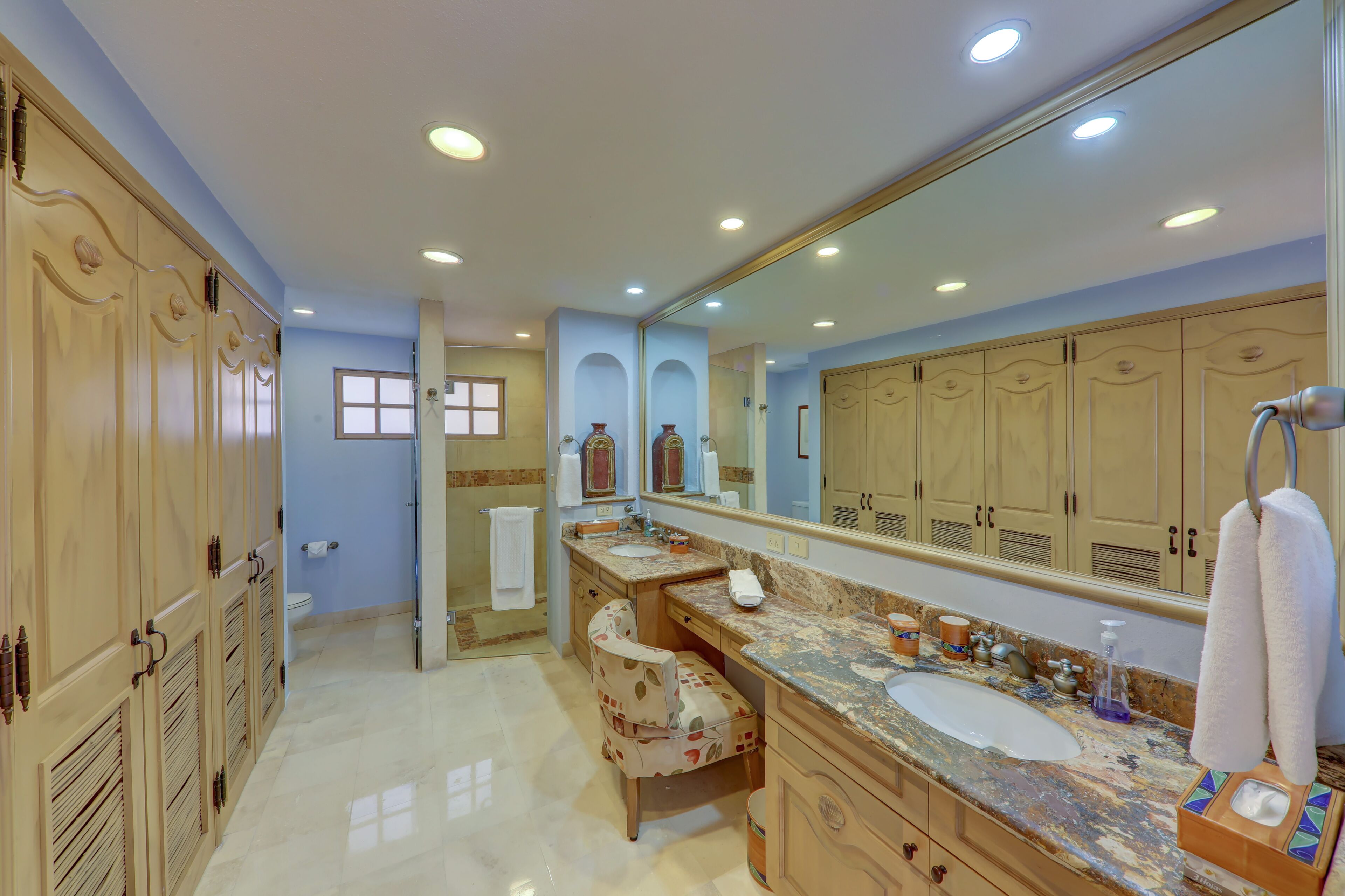 A bathroom with a large mirror, wooden cabinets, a marble countertop, and a shower area.