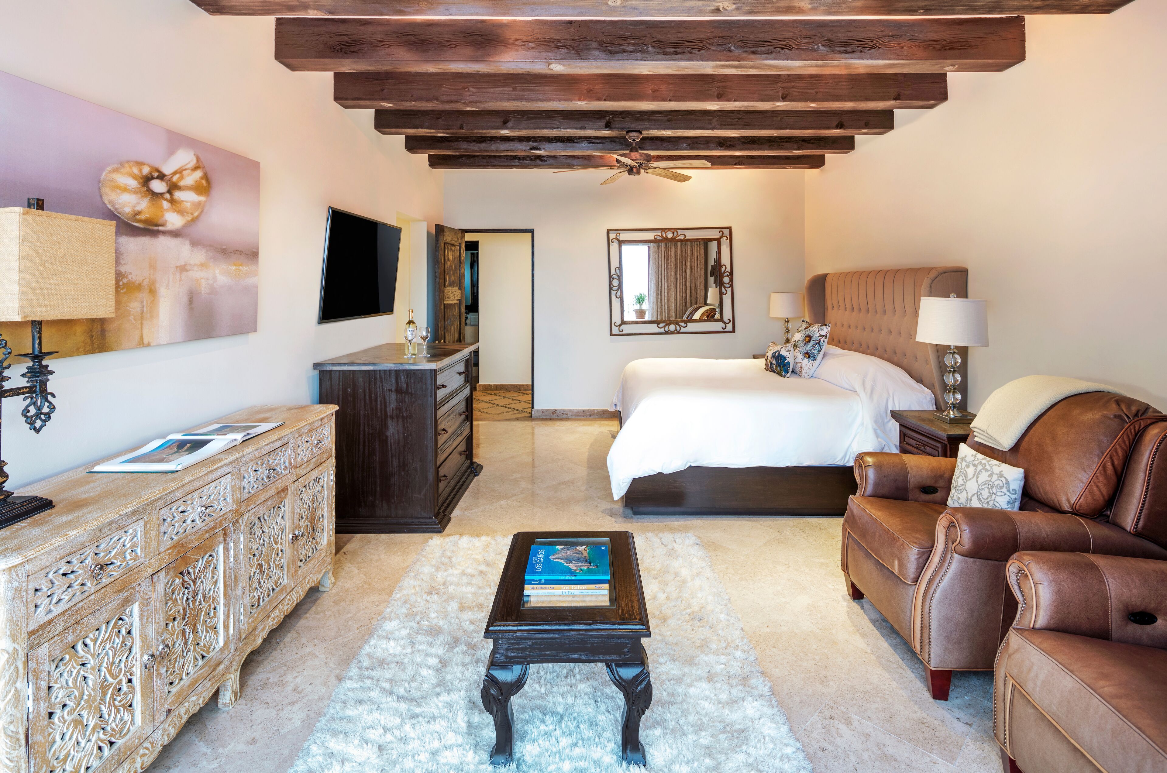A bedroom with a bed, a dresser, a coffee table, a sofa, a TV, and a ceiling fan.