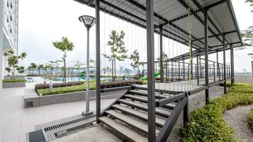 A covered outdoor staircase with metal railings, leading to a rooftop area with a view of a cityscape and a swimming pool.