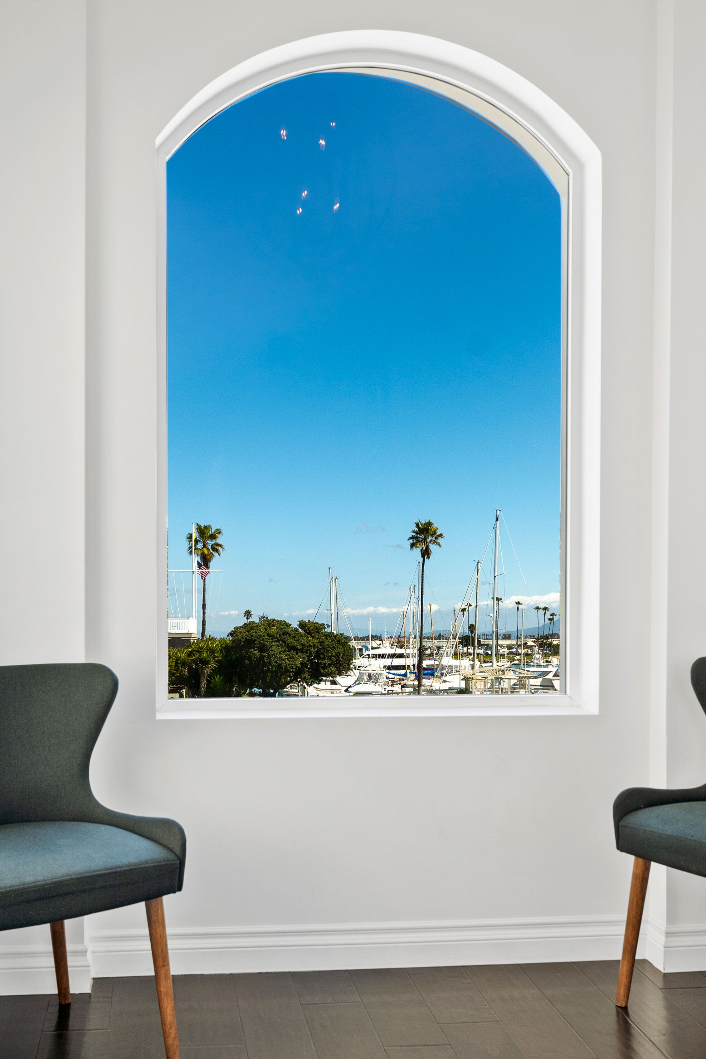 A room with a large arched window overlooking a marina with boats and palm trees.
