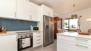 Una cocina moderna con armarios blancos, un refrigerador de acero inoxidable, un microondas y una mesa de comedor de madera con sillas.