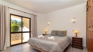 Un dormitorio con una cama grande, dos mesitas de noche con lámparas, un armario de madera y un ventanal corredero que da a un espacio exterior.