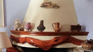 A cozy living room with a fireplace, a wooden mantel with decorative items, a stone wall, and a tiled floor. - L'Agrifoglio (Aritzo)