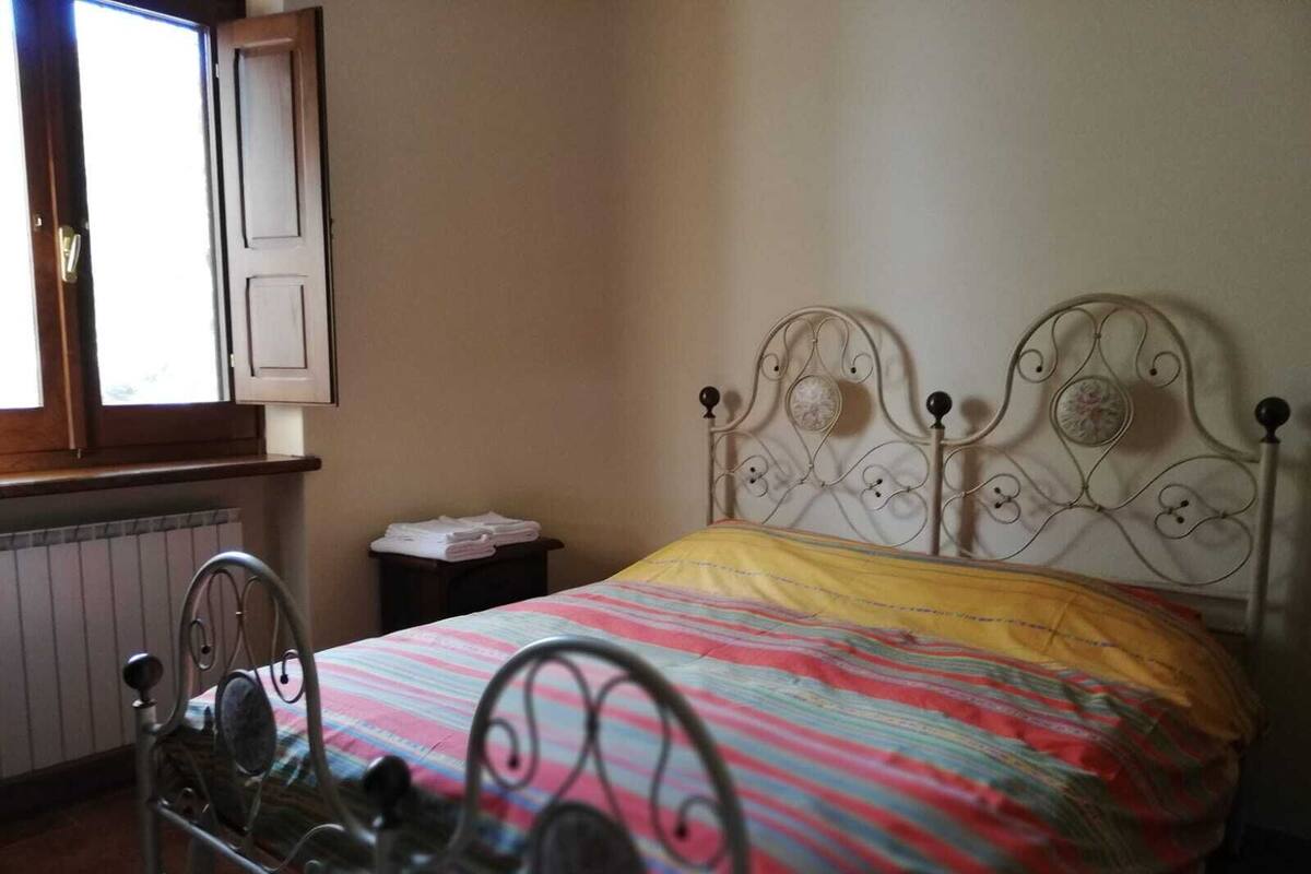 A bedroom with a metal bed frame, a window with shutters, and a radiator.