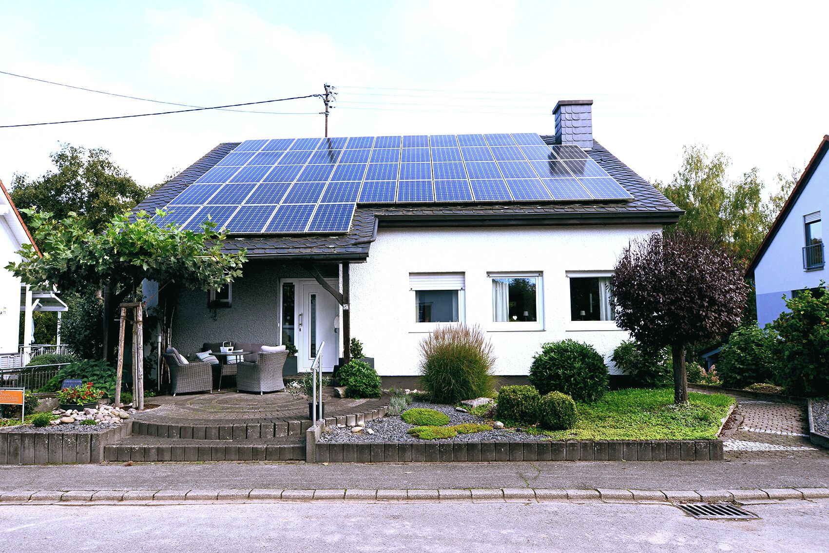 A house with a solar panel roof, a front porch with outdoor furniture, and a well-maintained garden.