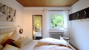 Un dormitorio con una cama grande, una ventana que ofrece vistas a zonas verdes, un radiador y un espejo en la pared.