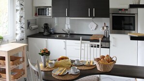Una cocina moderna con armarios oscuros, microondas, cafetera y una mesa de comedor con platos, tazas y una cesta de pan.