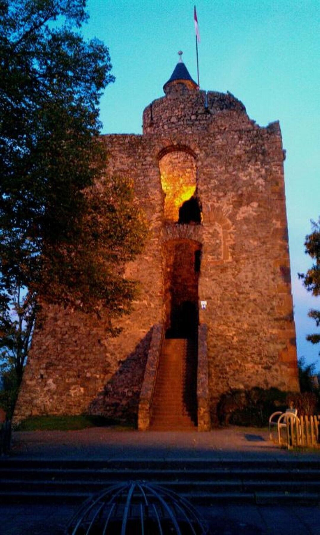 Eine steinerne Burg mit einem zentralen Turm, einer Flagge auf der Spitze und einer Treppe, die zum Eingang führt.