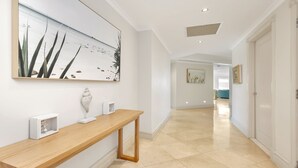 A hallway with a wooden console table, a large abstract painting, and a door leading to another room. - Unit 24 - 3 Bed Ocean View (TERRIGAL)