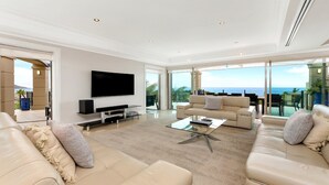 Ein geräumiges Wohnzimmer mit großem Flachbildfernseher, bequemen Sitzmöglichkeiten und einem Balkon mit Meerblick.