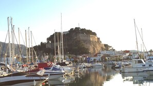 Un port de plaisance avec des bateaux amarrés, une colline rocheuse en arrière-plan et des bâtiments le long de la côte.