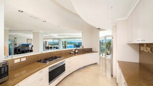 A modern kitchen with a curved island, built-in appliances, and a view of the outdoors. - Unit 36 - 4 Bed Platinum Ocean View (TERRIGAL)