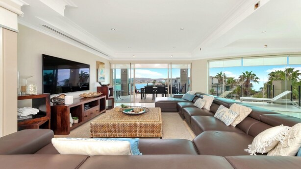 A spacious living room with a large flat-screen TV, comfortable seating, and a balcony with a view of the ocean. - Unit 36 - 4 Bed Platinum Ocean View (TERRIGAL)