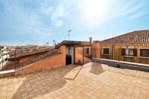 Una terrazza sul tetto con pavimento piastrellato, una piccola area chiusa con una porta e vista sullo skyline cittadino.