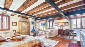 A spacious room with a large bed, wooden beams, a dining area, and a view of the city. - GuestHost - Exclusive studio perfect for 2 people and furnished in typical Venetian style overlooking the Canareggio Canal and Palazzo Labia. Location is strategic and convenient for those arriving in Venice: about 5 minutes walk from the train station a (Venezia)