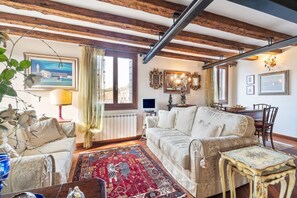 Ein Wohnzimmer mit einer Couch, einem Couchtisch, einem gemusterten Teppich und einem Essbereich mit Stühlen.