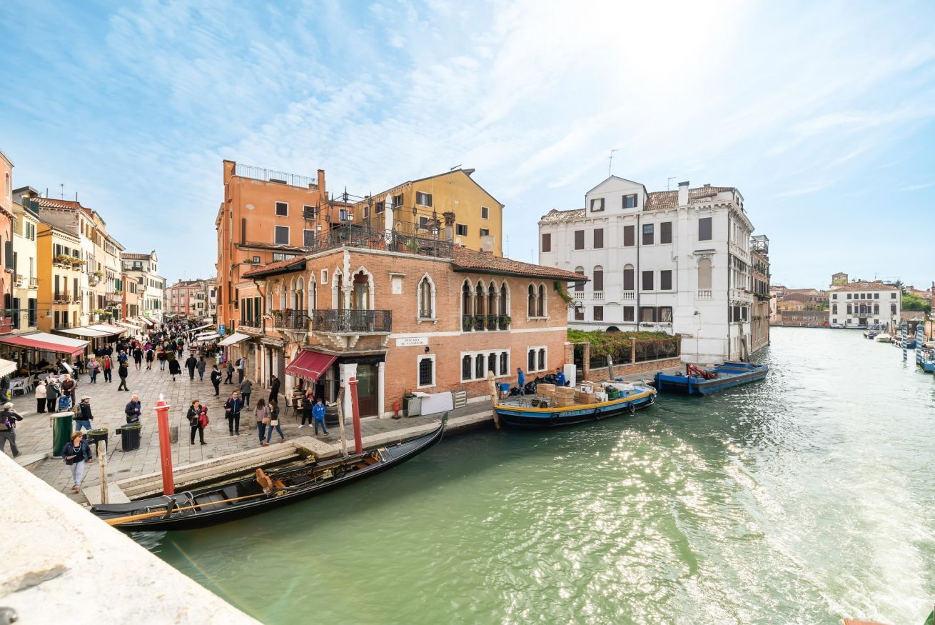 A canal with boats, historic buildings, and a crowd of people.