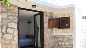 Una stanza con pareti in pietra, un letto, una finestra con persiane e un piccolo balcone.