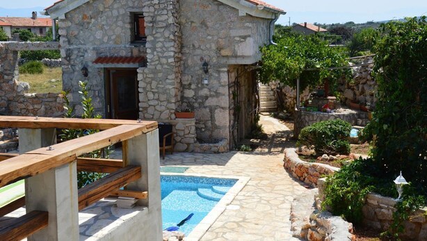 Un edificio in pietra con tetto in tegole, una piscina e un pontile in legno.