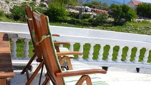 Una sedia di legno con un cuscino verde su un balcone che si affaccia su un panorama con montagne e un lago.