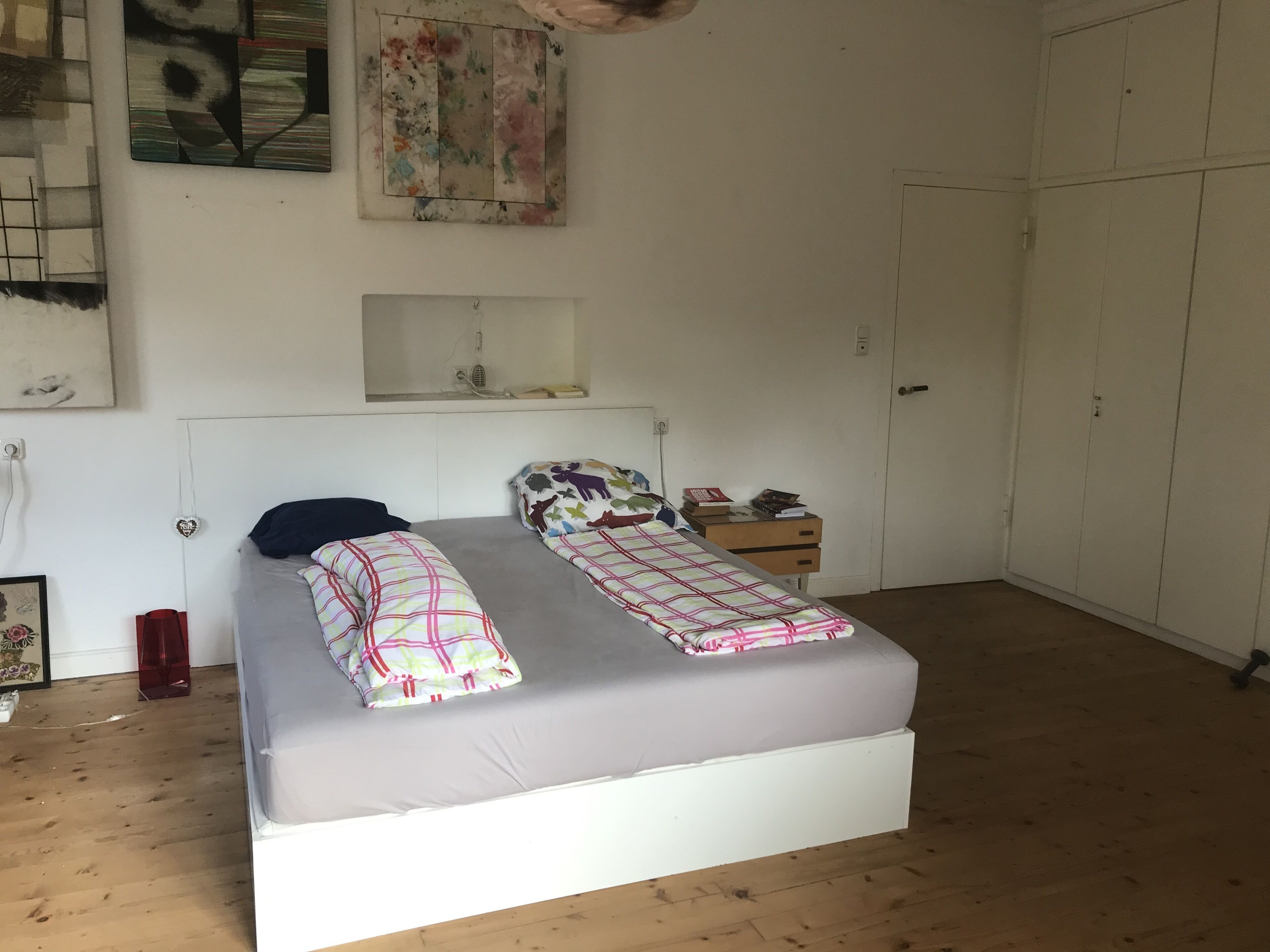 A bedroom with a bed, a nightstand, a wardrobe, and a wall-mounted shelf.
