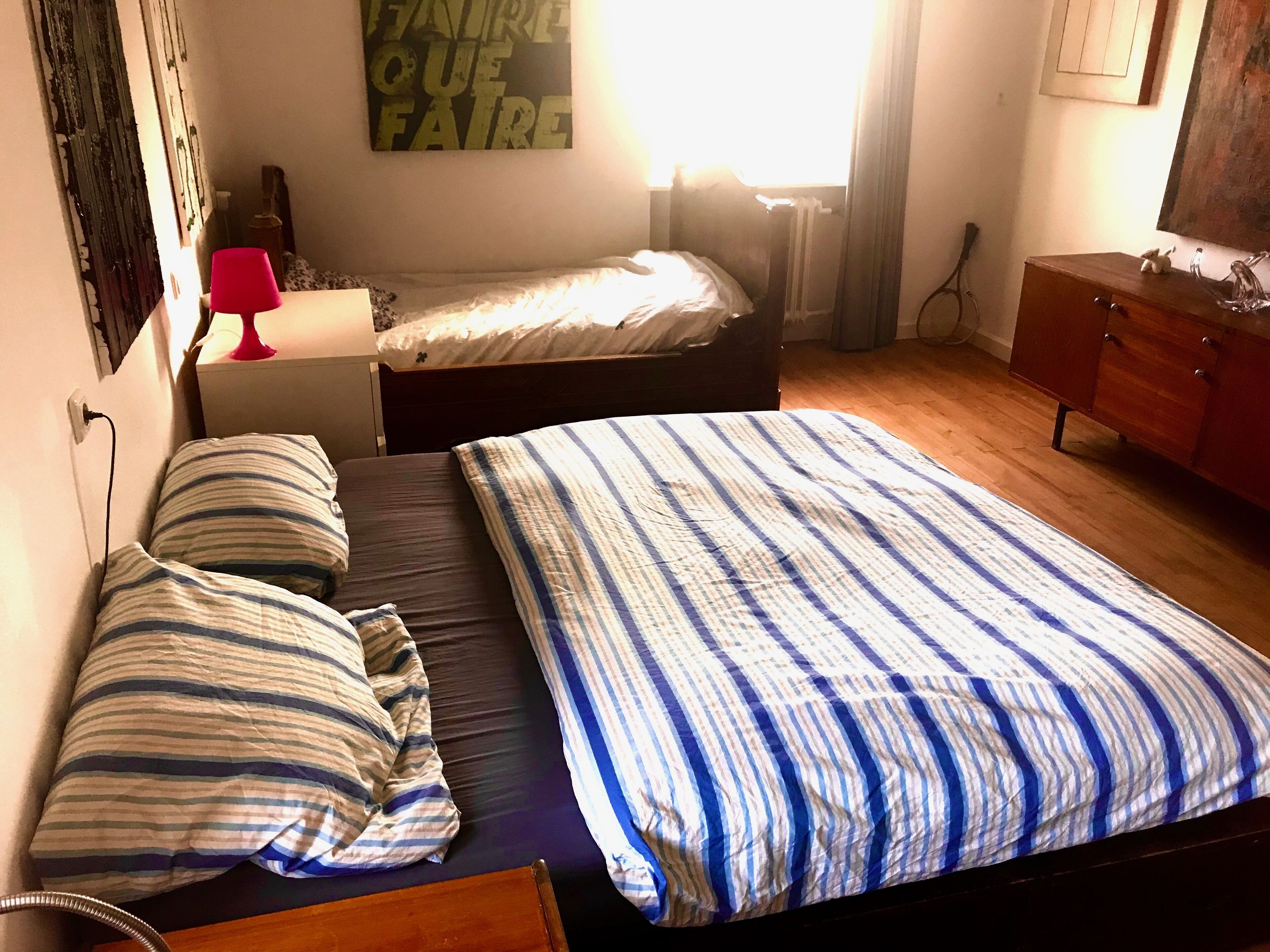 Un dormitorio con dos camas, un aparador de madera, una mesita de noche y una pared con una cita inspiradora.