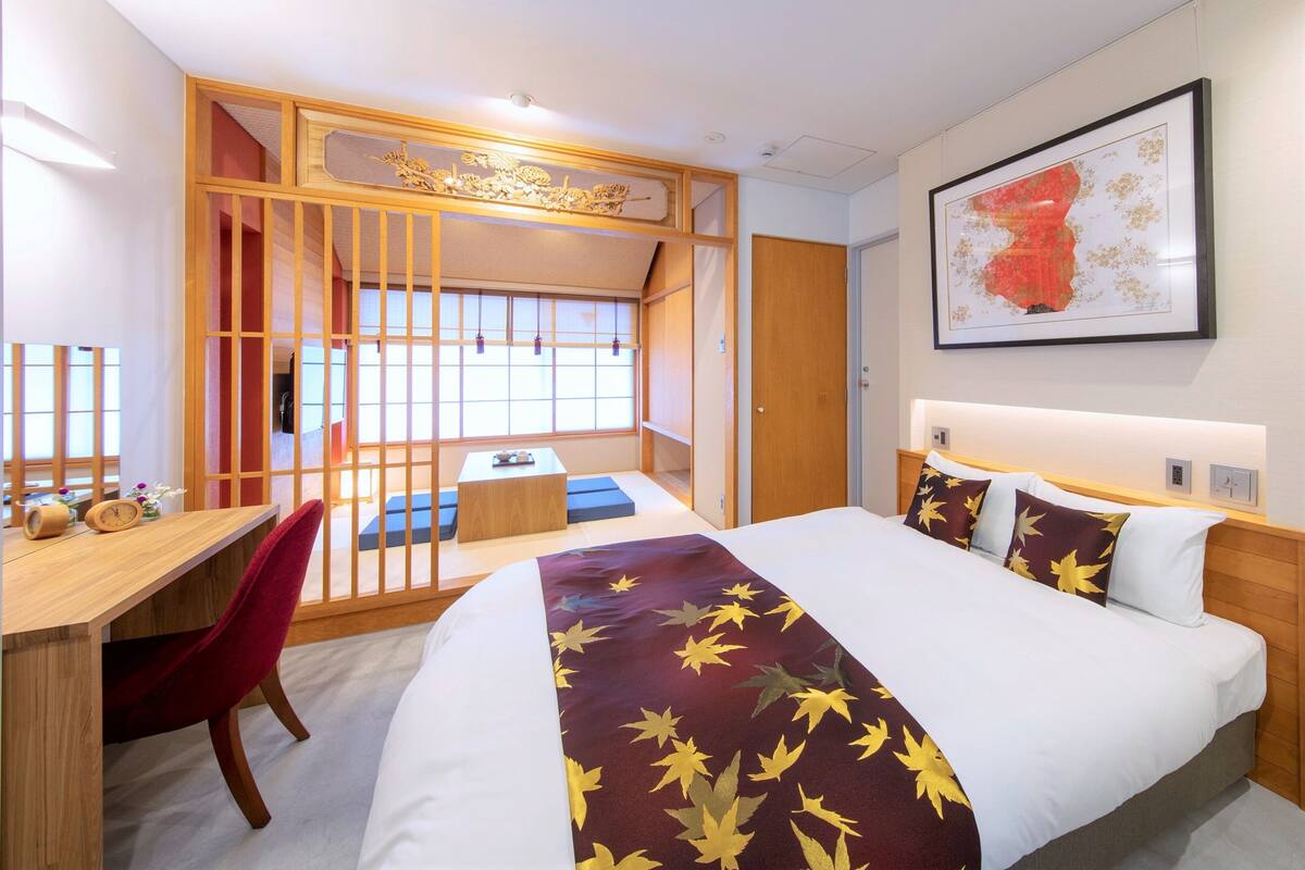 Une chambre d’hôtel avec un lit, un bureau, une chaise, une fenêtre et un tableau encadré au mur.