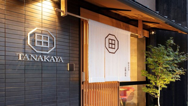 Un bâtiment moderne à la façade sombre, doté d’une entrée en bois et d’une enseigne portant l’inscription « TANAKAYA ».