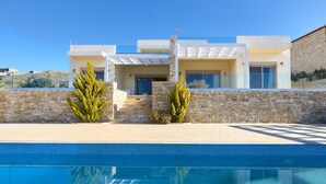 A modern house with a swimming pool, stone walls, and a clear blue sky. - Elkysti Crete (Faistos)