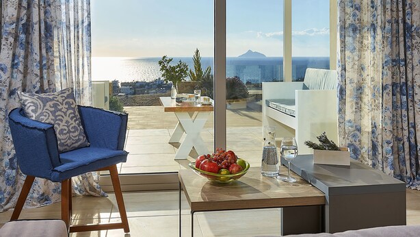 A modern living room with a view of the sea, a blue chair, a table with a fruit bowl, and a white letter 'X'. - Elkysti Crete (Faistos)