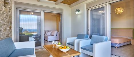 A modern outdoor seating area with a wooden table, white sofas, and a view of the sea.