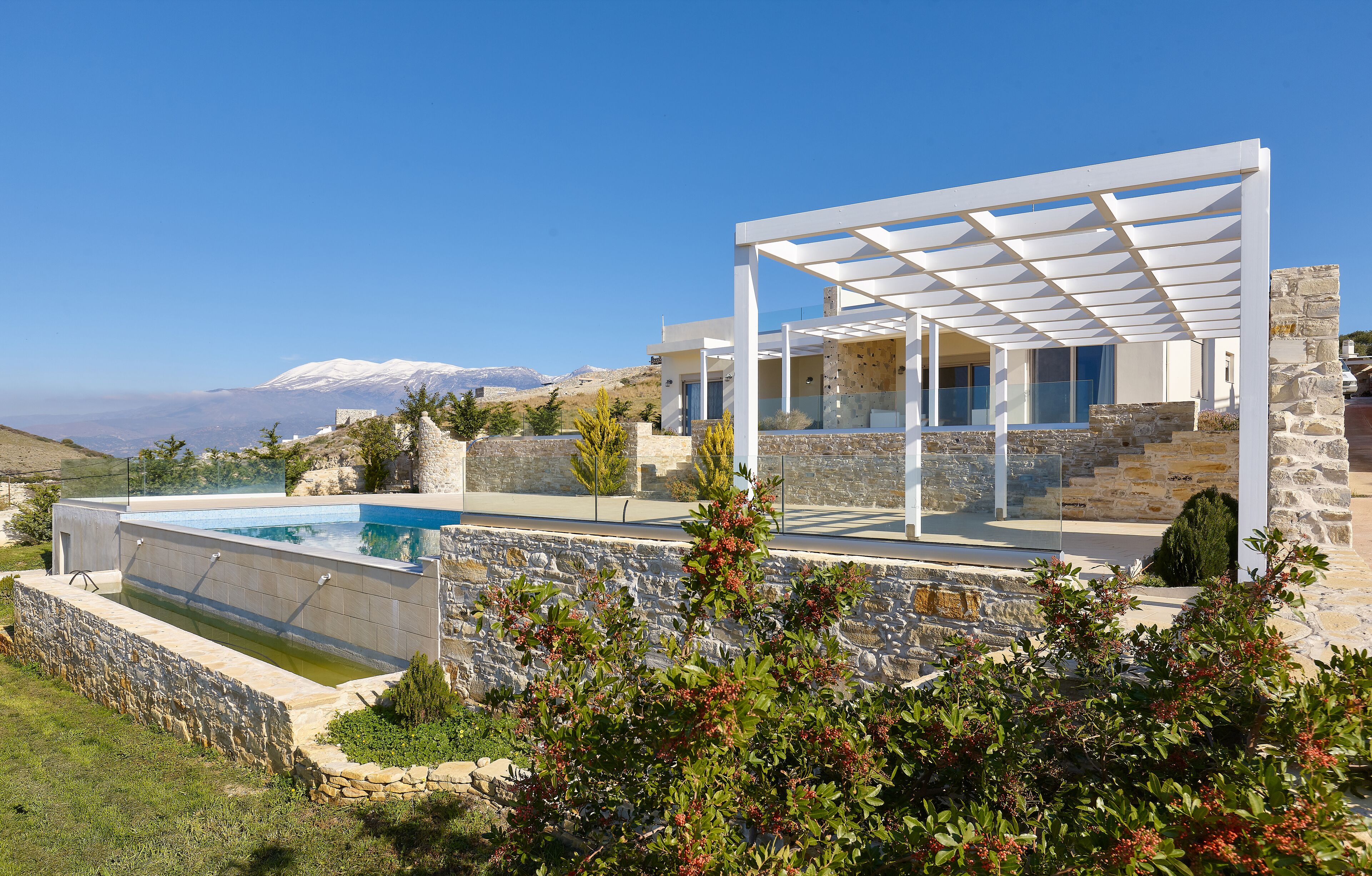 Une maison moderne avec une piscine, des murs en pierre et une vue sur les montagnes.