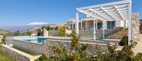 Une maison moderne avec une piscine, des murs en pierre et une vue sur les montagnes.