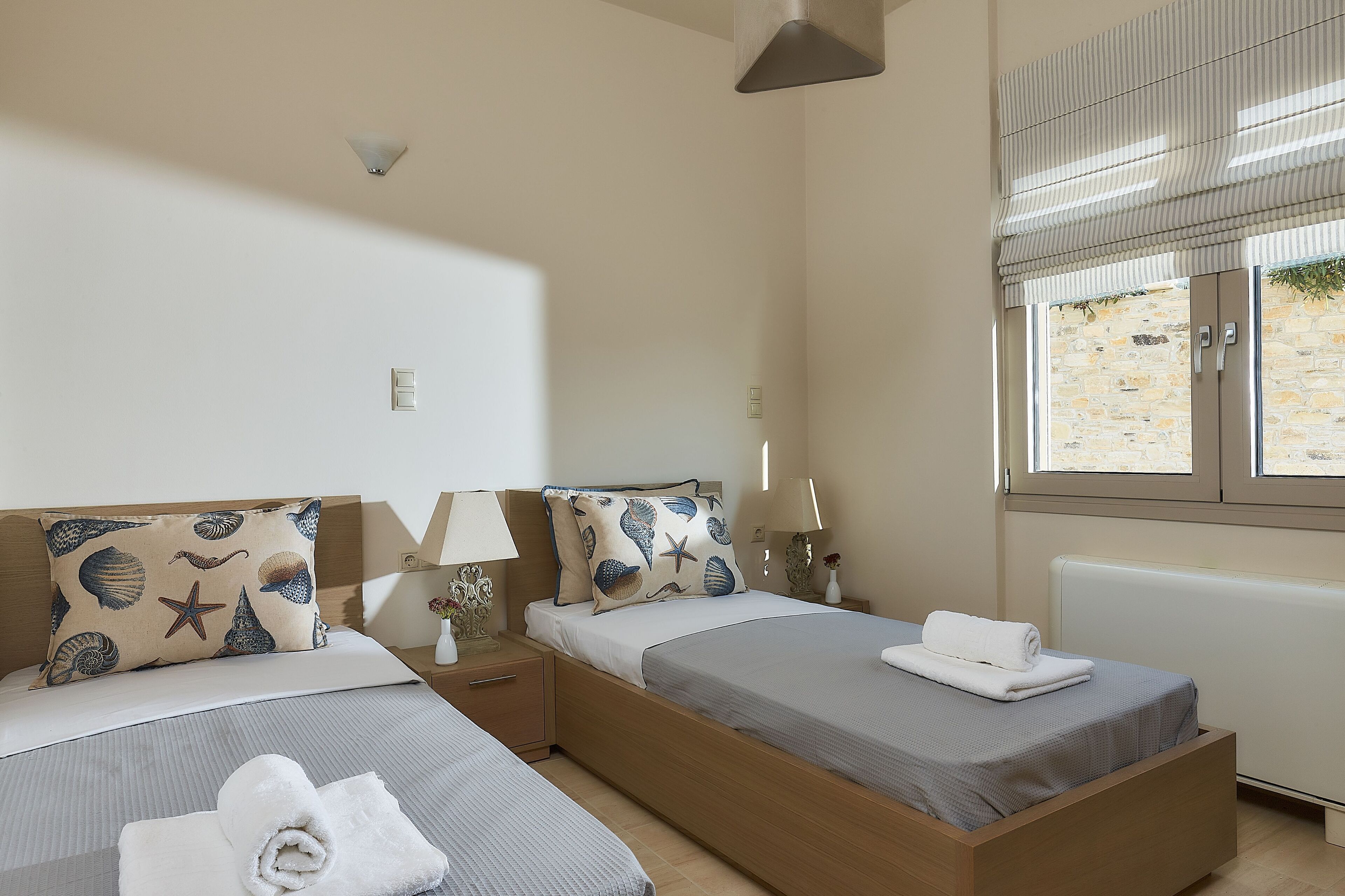 A bedroom with two beds, a window with blinds, a lamp, and a starfish pillow.